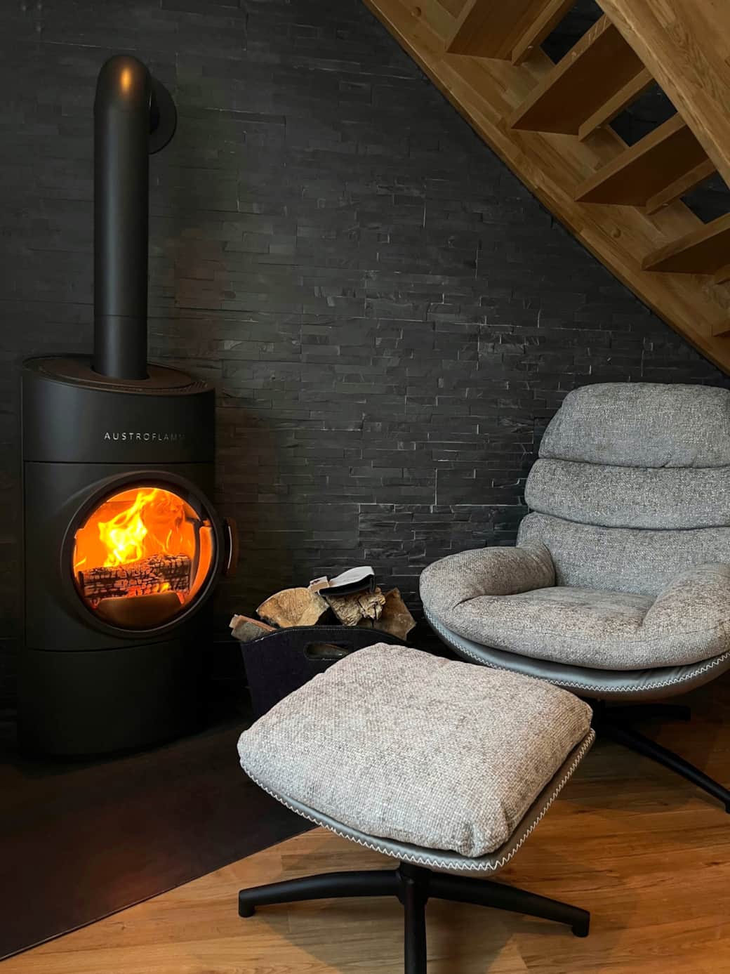 Kaminmomente pur: Flackerndes Feuer vor der Natursteinwand, daneben ein gemütlicher Sessel.