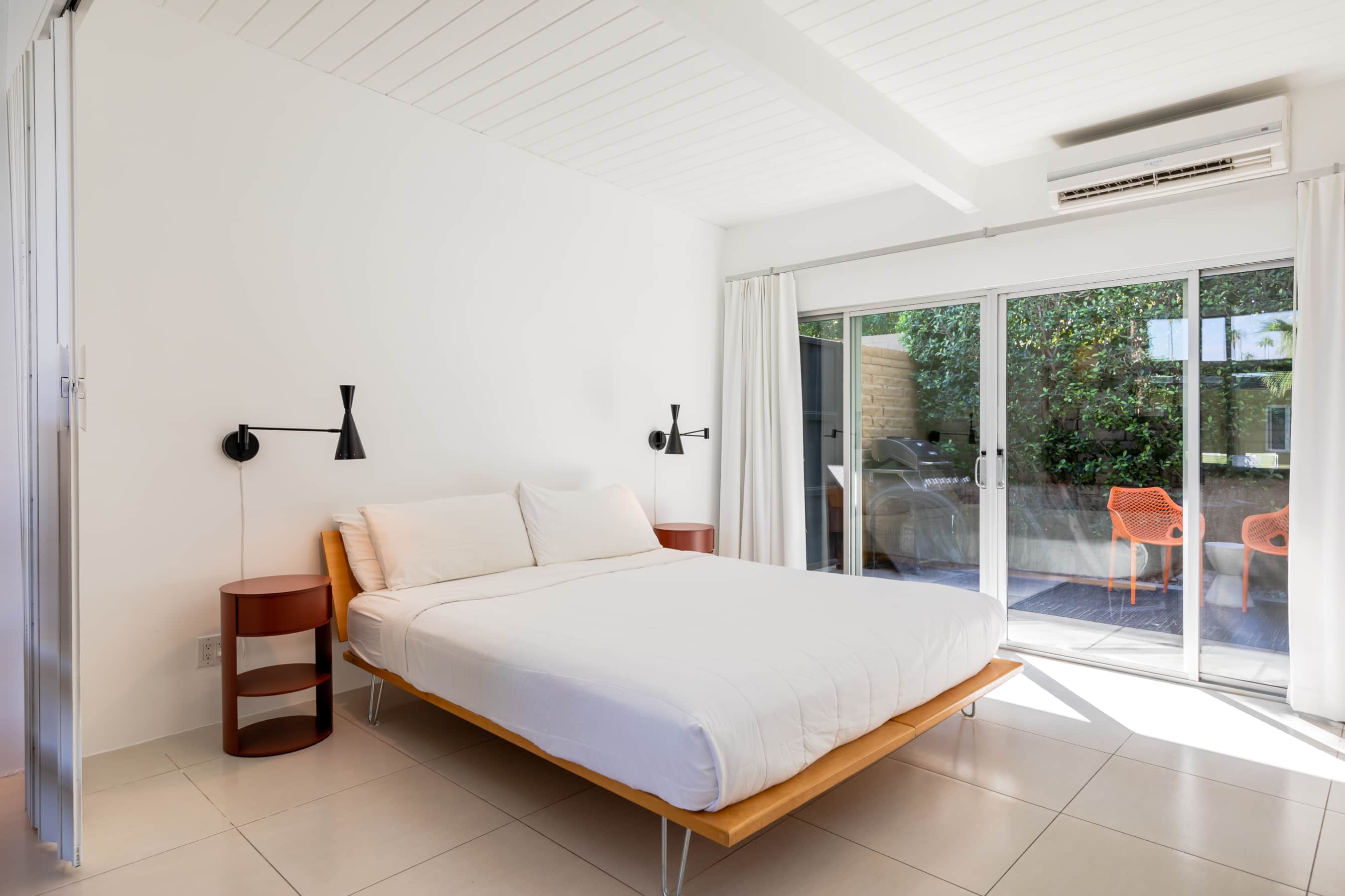 A white room with a bed, nightstands, and sliding glass doors leading to a patio.