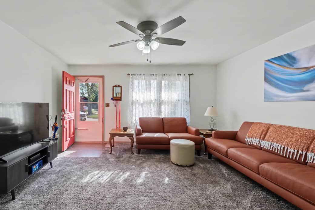 Living room with seating for 6, a recliner and a large Roku TV. Hallway to the bedroom on the right.
