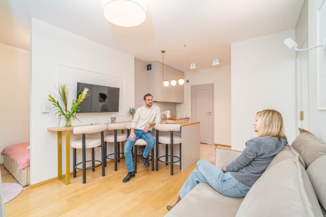 Przytulny salon z aneksem kuchennym, stołem barowym i sofą w jasnej, nowoczesnej aranżacji.