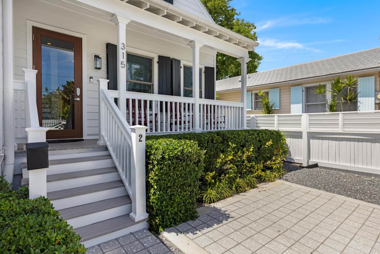 The charming exterior of the house, showing its white facade and a paved driveway.