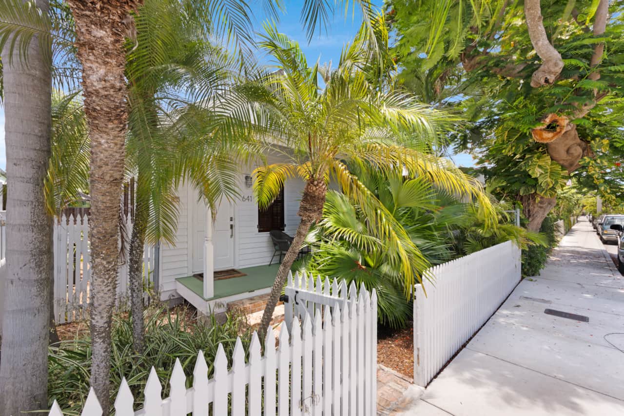 Street view of classic Key West cottage with white picket fence and palms.