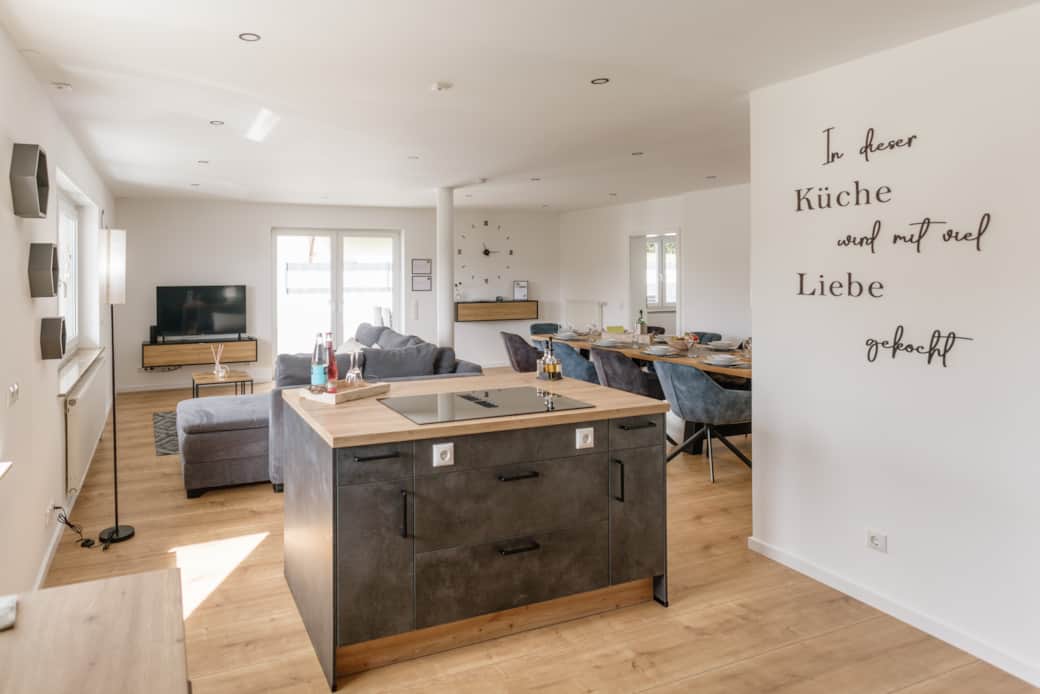 Offener Wohnbereich mit Kochinsel, Küche, Wohnzimmer und Essbereich mit Tisch für 10 Personen.
