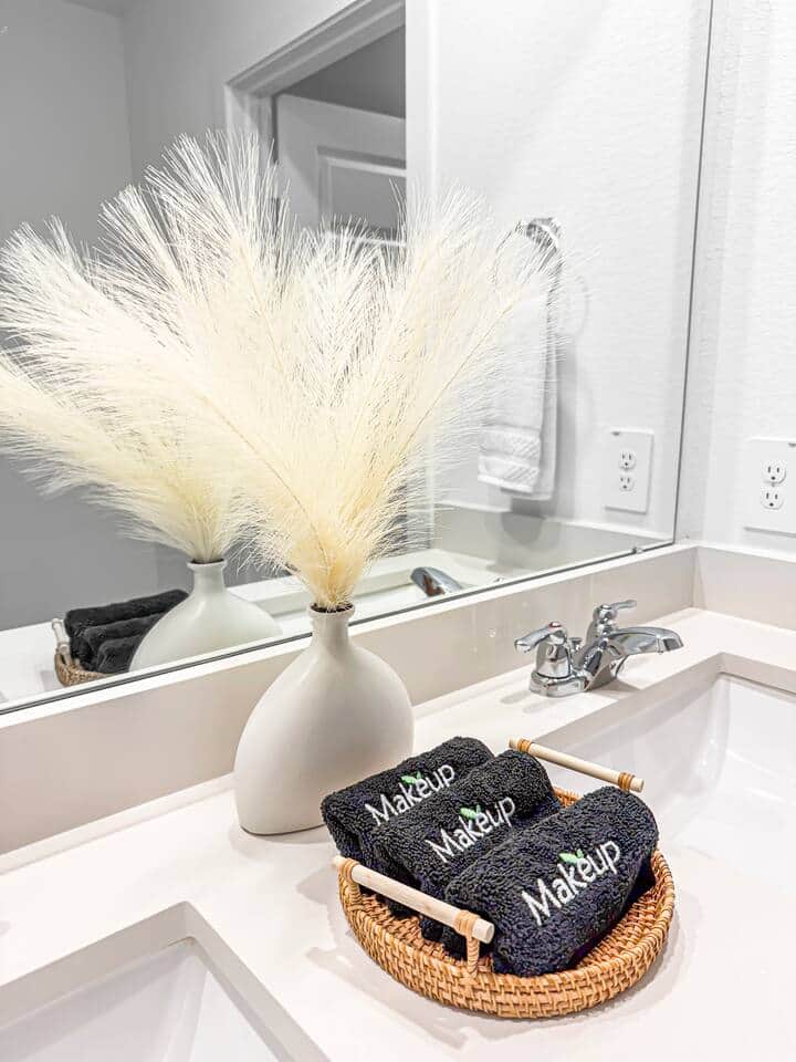 Large mirror sitting on top of double sinks and faucets. Enjoy the black makeup towels for your facial needs.