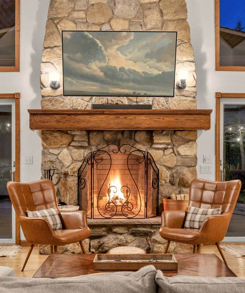 Relax in the elegant living room featuring a vaulted ceiling, grand stone fireplace, and cozy seating. Warm and inviting, it's the perfect space to unwind, connect, and enjoy the morning and evening passing of deer alongside the property.