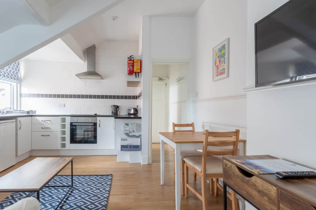 Light and airy living area with sofa, smart TV, dining table and kitchen.