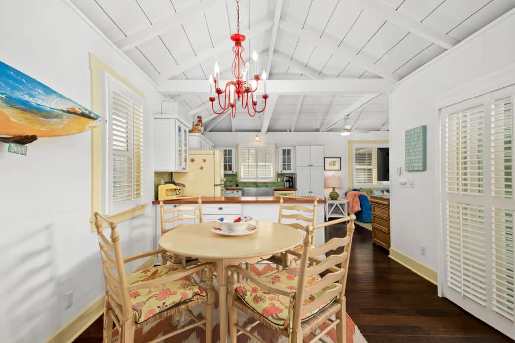 Sunny cottage dining with red chandelier, tropical seats, and vintage kitchen.
