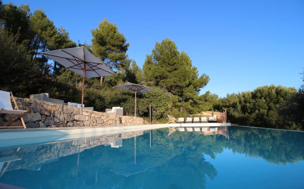 Piscine à débordement, totalement privée. On voit la maison dans le fond. terrasse aménagée sur une restanque, à flanc de colline. Grands parasols Vlaminck.