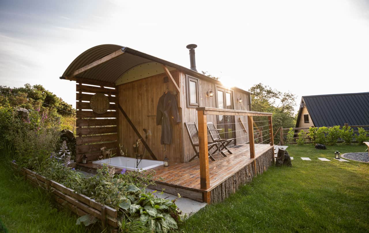 Rustic hut with deck and outdoor bathtub at sunset