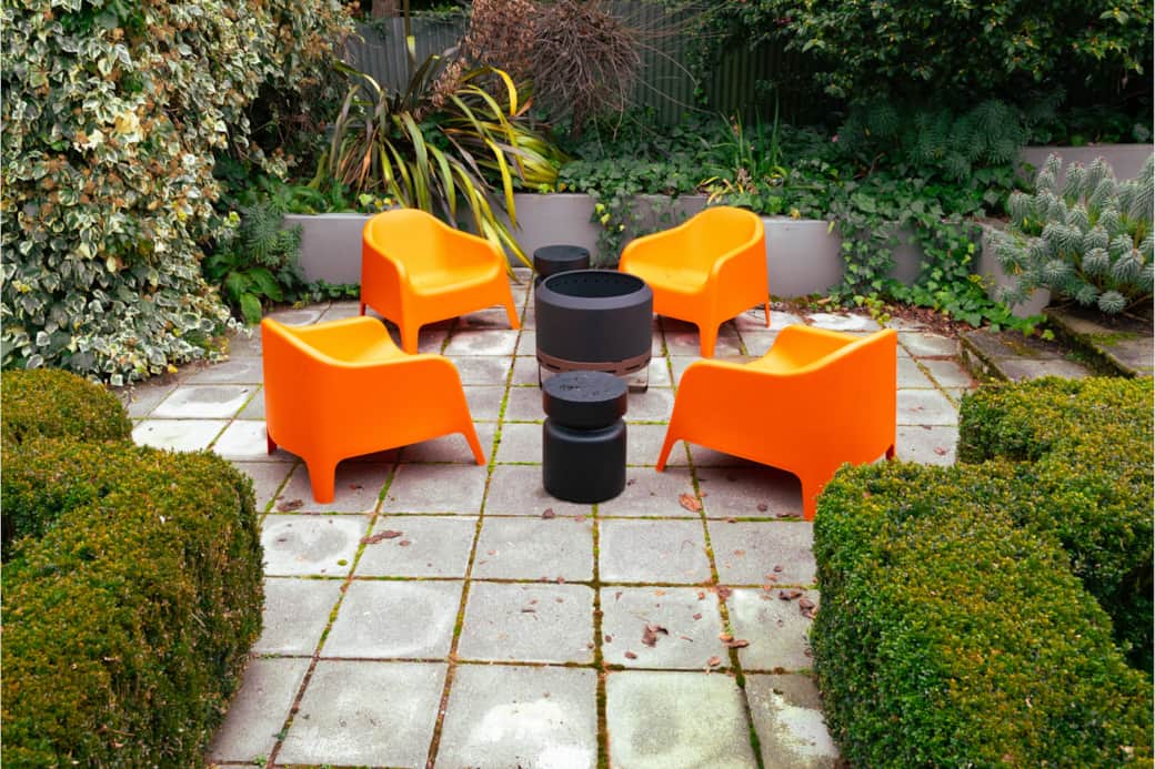 Chilled patio with burnt orange loungers, firepit, coffee tables, and lush green gardens.