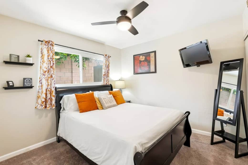 Space includes wall-mounted TV, ceiling fan with light, and full-length mirror for comfort.