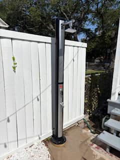 Outdoor shower in a private courtyard at a Galveston vacation rental, surrounded by greenery and privacy fencing