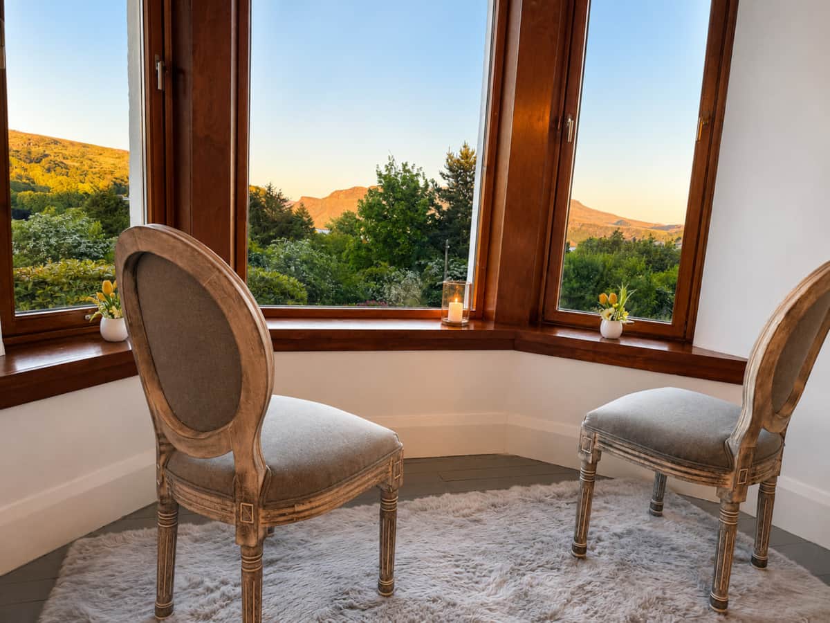 A pair of French-style chairs in the dining room bay window at sunset.