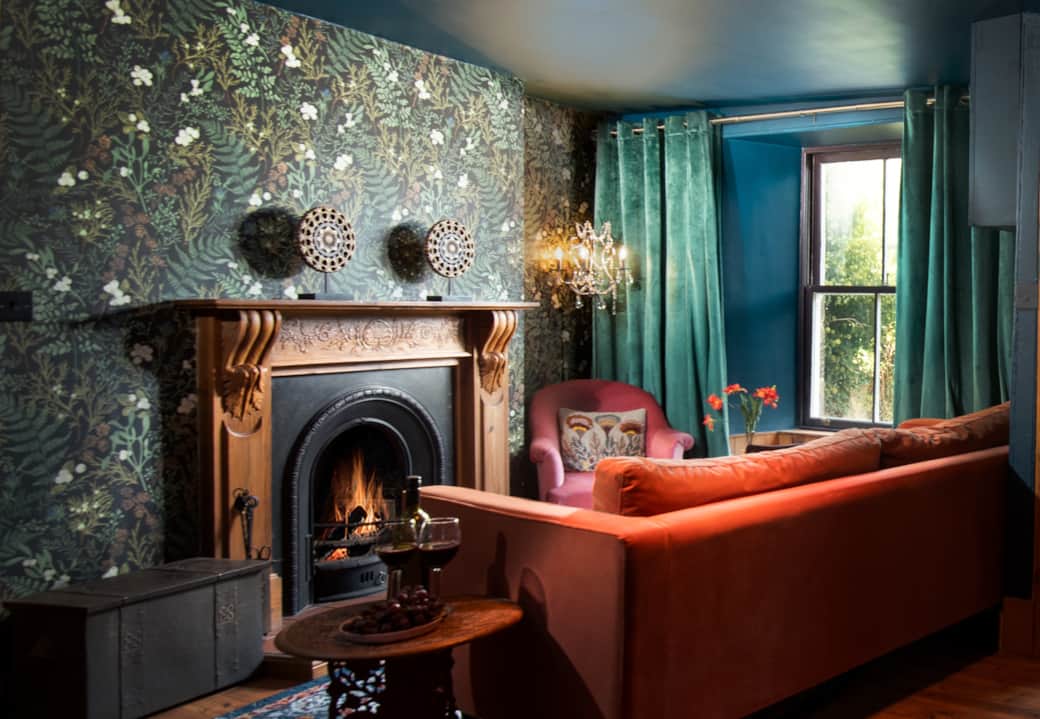 Eccentric Caterpillar lounge: Teal/blue walls, velvet sofa, fireplace, and cozy reading nook.
