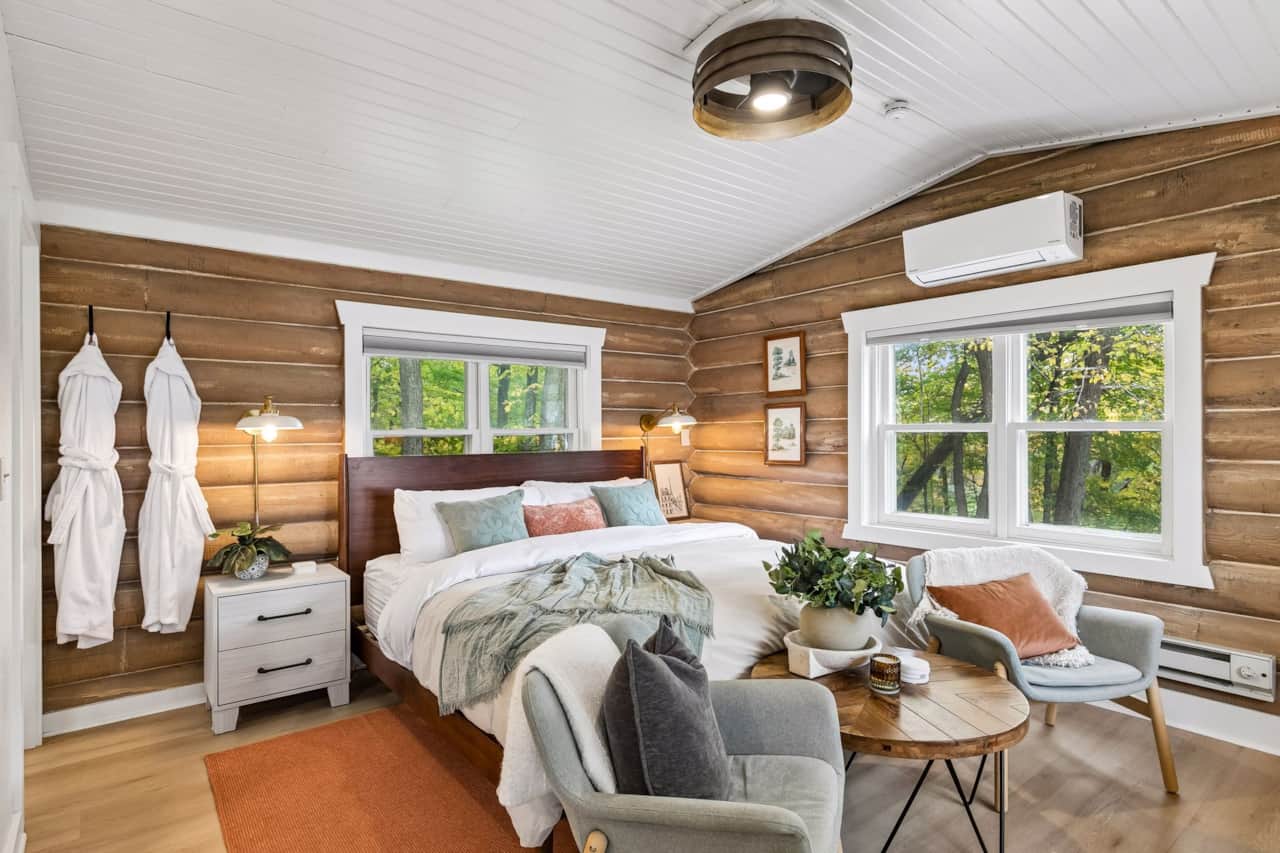 King bed under the white plank ceiling. Robes on the hooks, woods out every window.