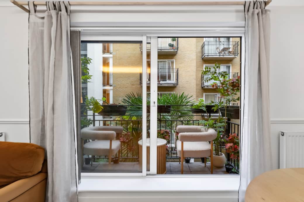 Balcony view through sliding doors with outdoor seating and greenery, offering a peaceful courtyard Balcony view through sliding doors with outdoor seating and greenery, offering a peaceful courtyard
