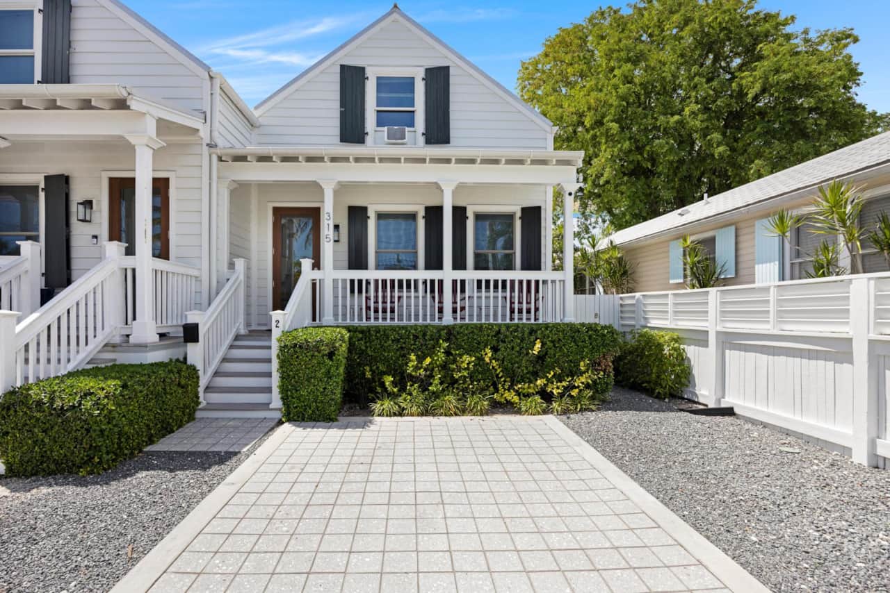 The charming exterior of the house, showing its white facade and a paved driveway.