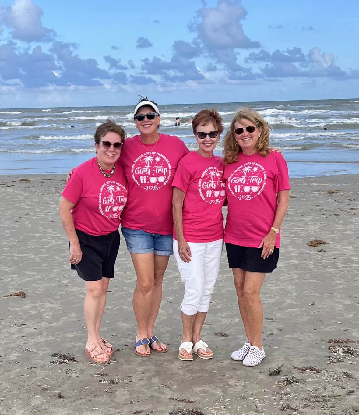 Group of women wearing matching girls trip shirts on the beach in Galveston