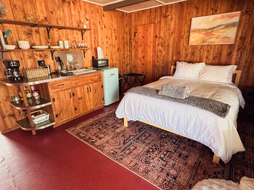 Rustic wood-paneled room with queen bed, kitchenette, and vintage mini fridge