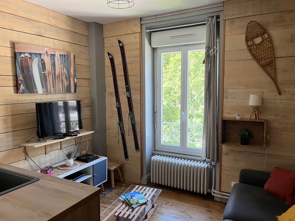 Ambiance montagnarde charmante avec skis anciens, luge-table basse et déco boisée. Vue sur la nature, TV, lumière douce et coin cosy. Parfait pour se détendre après une journée au grand air au Mont-Dore.