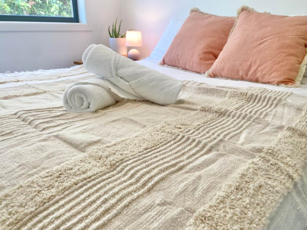 Queen bed dressed in soft linen with rolled towels and cushions