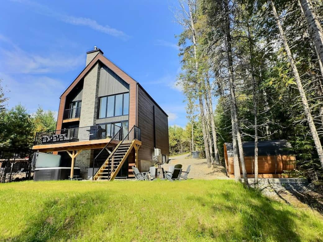 Summer view of Villa Forêsta with hot tub, sauna & forest backdrop.