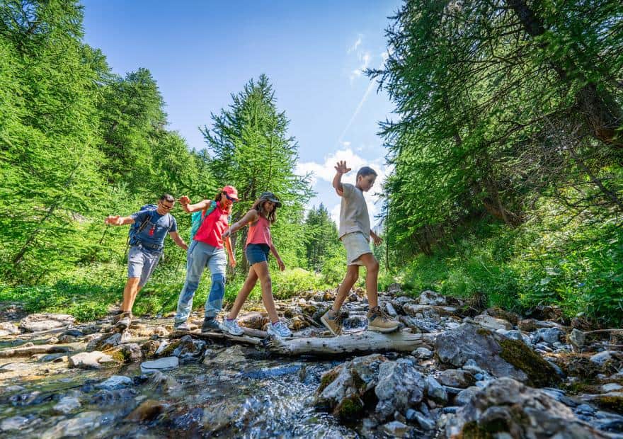 Famille en randonnée traversant un torrent de montagne en été, Serre Chevalier Vallée