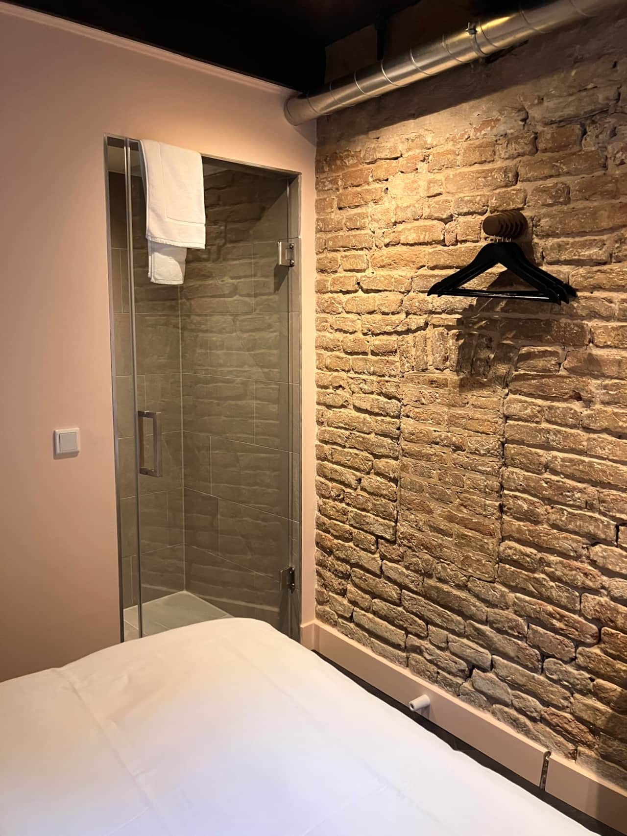 Robinah Suite bedroom with a glass-walled open shower against exposed brick