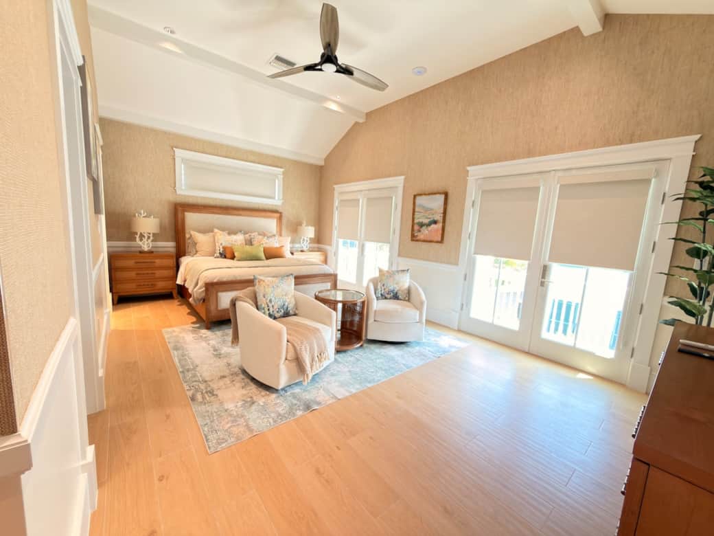 A spacious upstairs primary suite with a king bed, vaulted ceiling, smart TV, ceiling fan, and a private sitting area. Finished in a refined coastal-modern style, it also features a private balcony overlooking the pool and a luxurious en-suite bath.