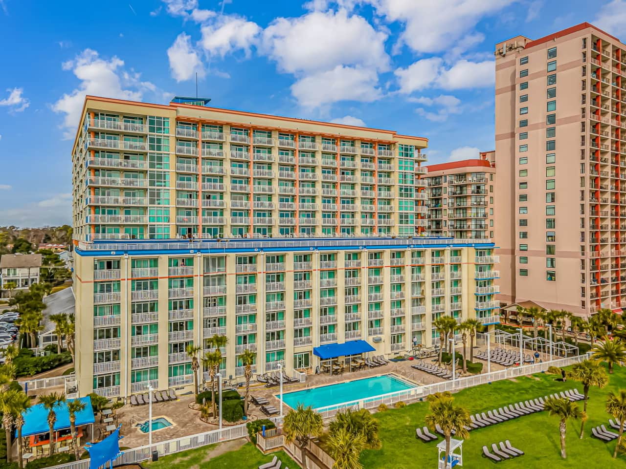 Resort Towers & Oceanfront Pool Deck Bright resort exterior with large pool deck, loungers, and dire