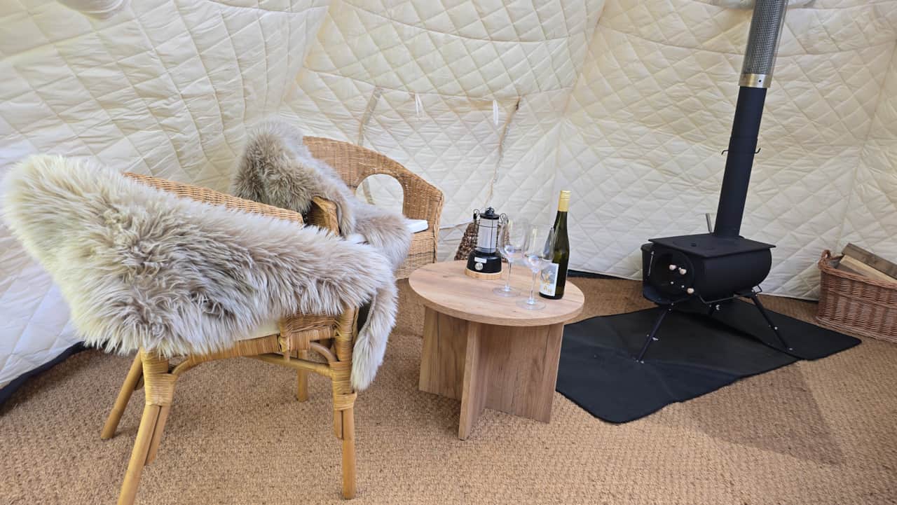 Lounge area with sheepskins, wine for two and a wood stove in the glamping tent