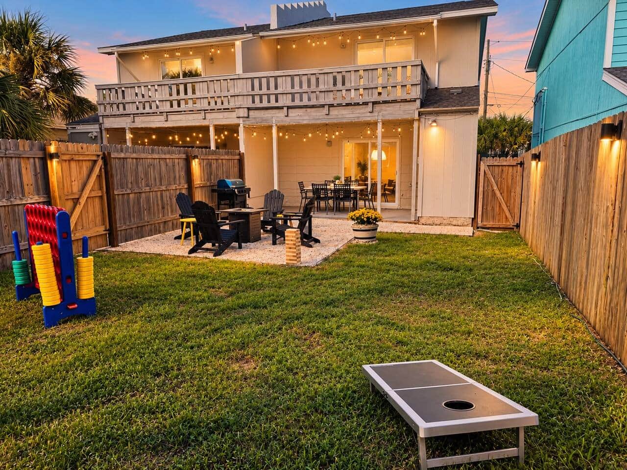 Two levels of outdoor living in Unit B: a covered dining patio downstairs and a private balcony off the upstairs king suite. The fenced yard includes a fire pit, lawn games, and BBQ grills, with a gate connecting to Unit A's backyard