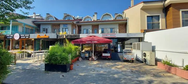 Street view of Apart Guney 7 with nearby shops and a red canopy, Göcek.