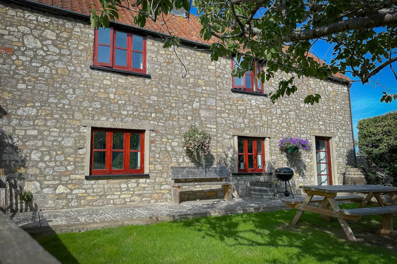 Inglenook's enclosed garden with large picnic bench, BBQ, patio door leading from the living room