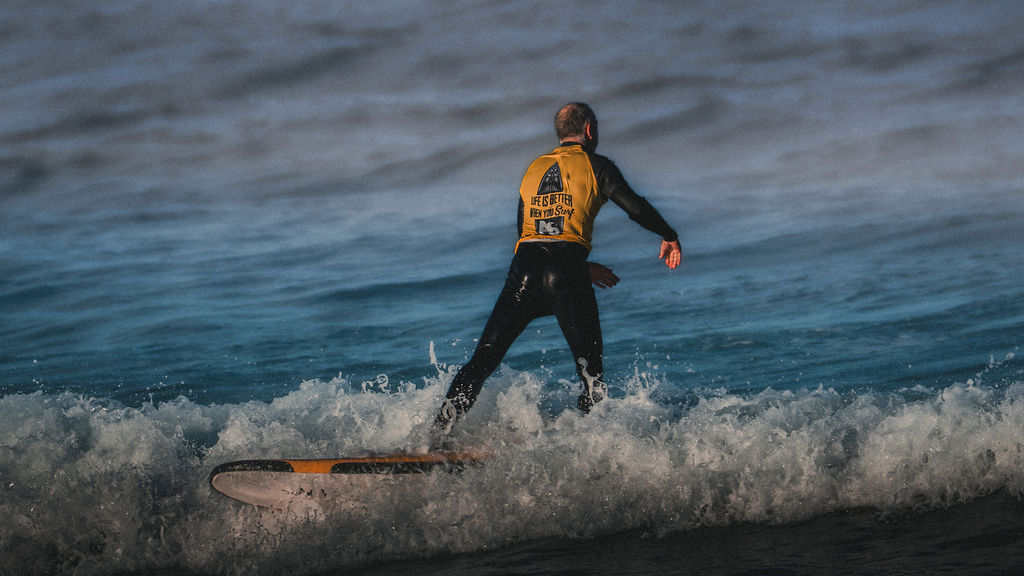 Ein Surfer im Neoprenanzug steht auf dem Brett im Weißwasser einer Welle