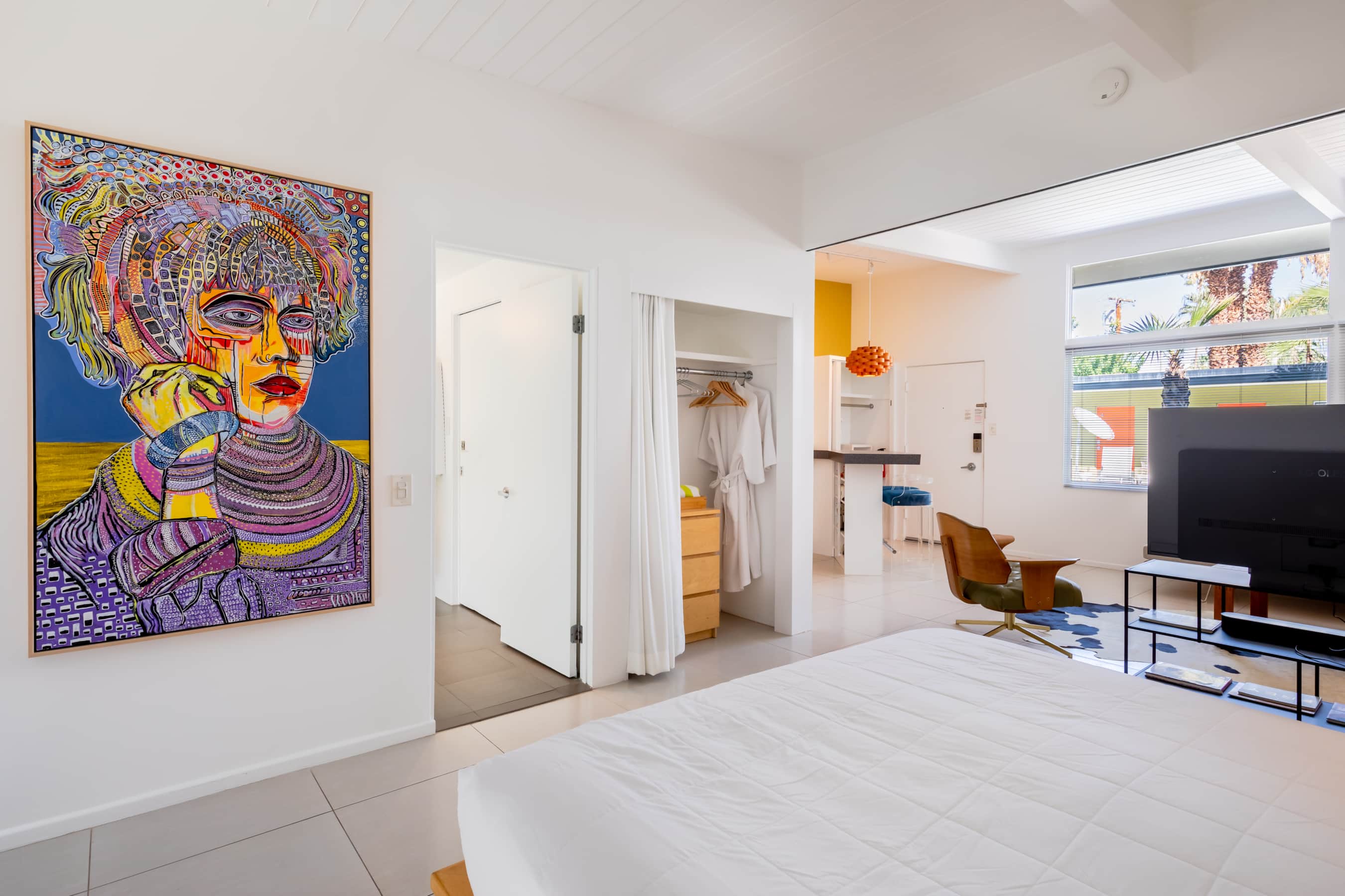 A wide view of a studio room with a large bed, a colorful artwork on the wall, and a TV on a stand.