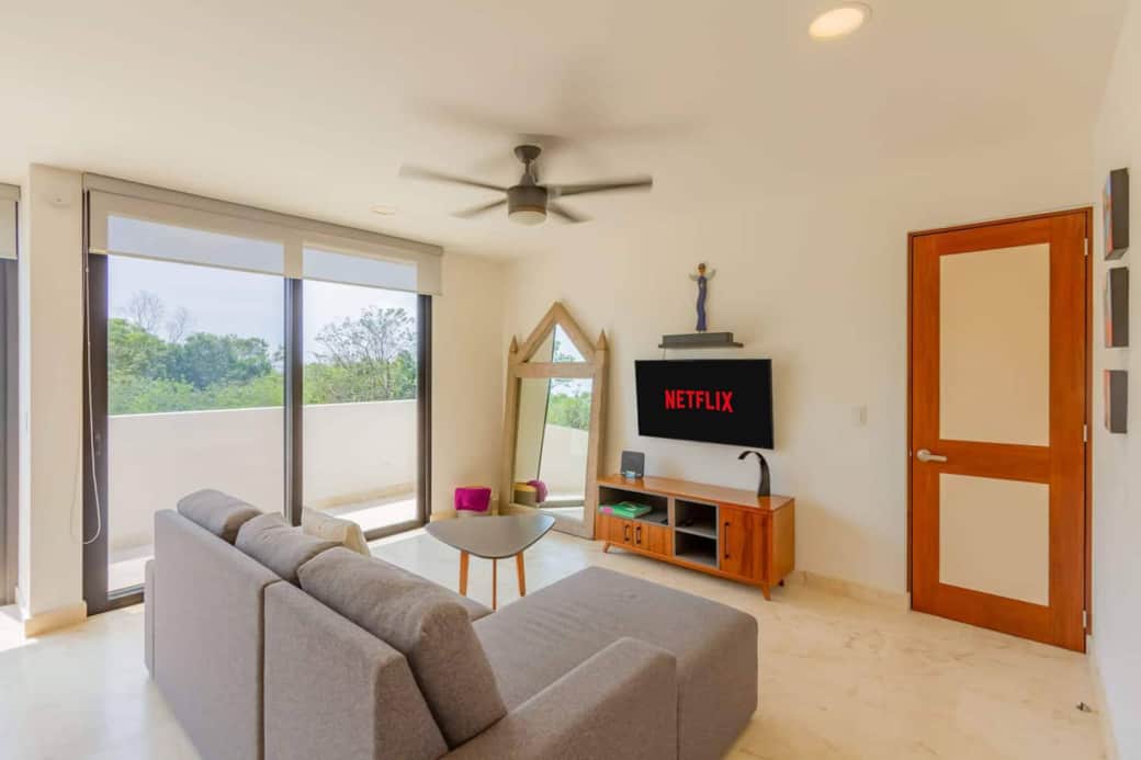 Relax in a bright, comfortable living room with a 55” Smart TV, A/C, and ceiling fan. Step out to your private balcony and enjoy peaceful jungle views, while room-darkening shades add privacy and comfort for relaxing day or night.