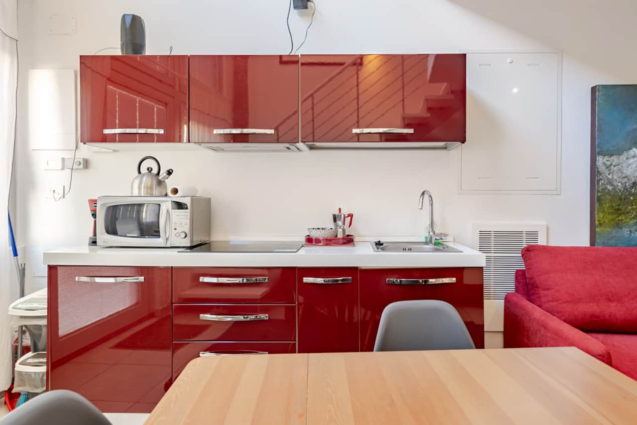 Küche mit roten Möbeln, Mikrowelle und Sofa neben dem Tisch