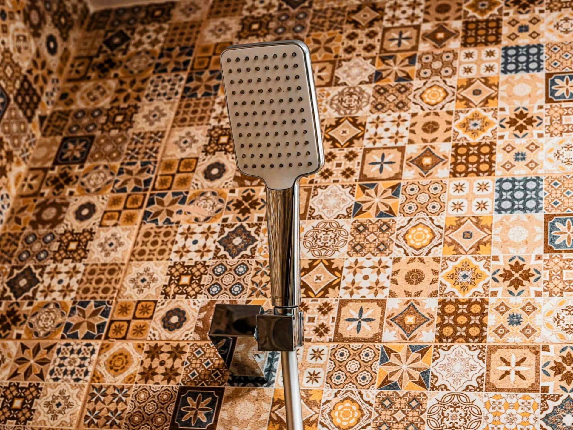 Ducha moderna con rociador rectangular y pared de azulejos decorativos en tonos tierra y geométricos