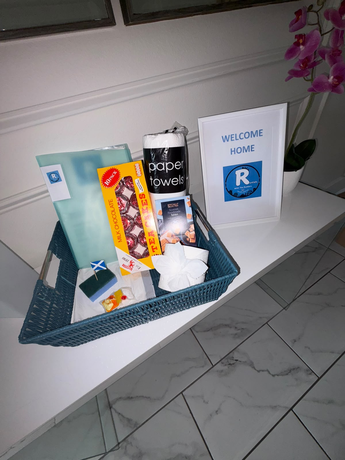 Rudders Rentals welcome basket with Tunnock's teacakes, tablet and a Welcome Home sign