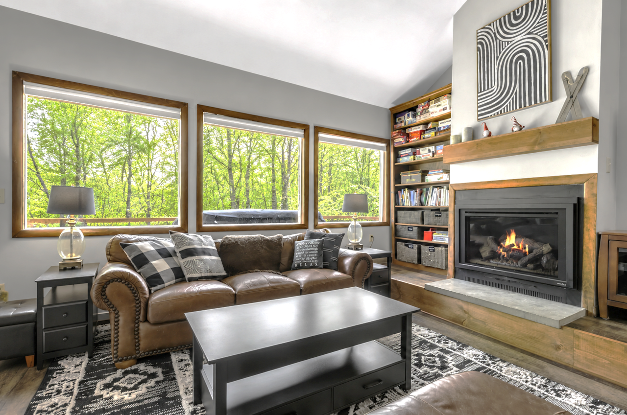 Bright living room with panoramic forest views, fireplace, games, and relaxing lodge feel