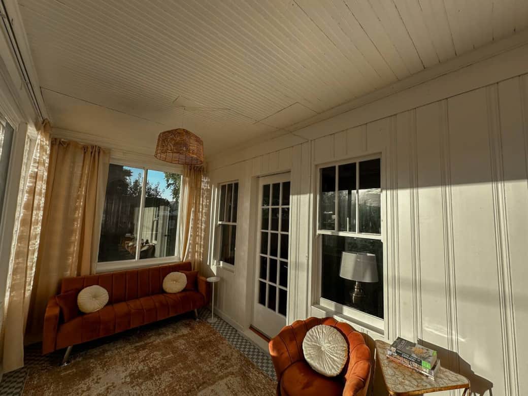 Sunroom filled with natural light, featuring warm tones, vintage-inspired seating, and soft curtains. A perfect spot to sip coffee, read, or enjoy peaceful morning sunlight in a cozy, inviting atmosphere.