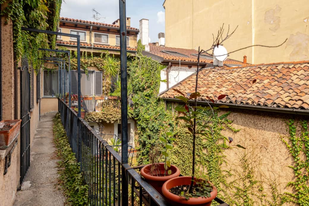 Laubengang mit Geländer und Pflanzkübeln über einem Innenhof mit Kletterpflanzen und Ziegeldächern, in Brera, Mailand