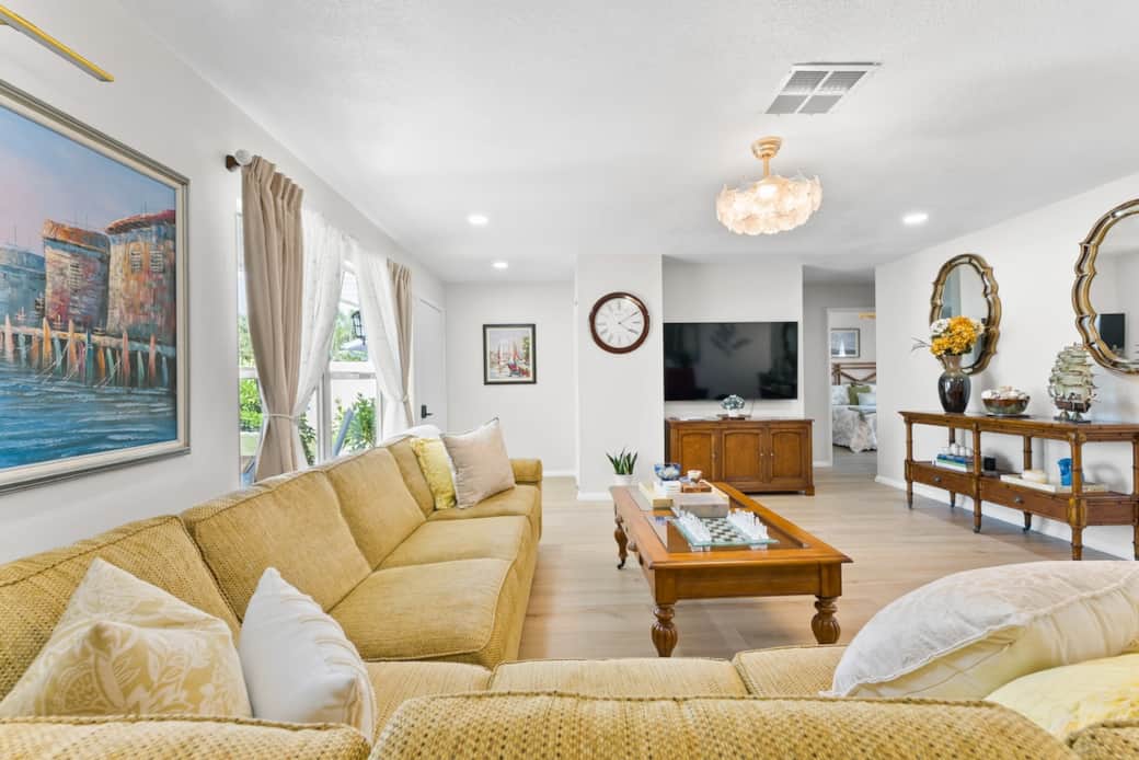 Oversized windows fill the room with natural light, highlighting the warm coastal decor, light wood looking tile flooring, and elegant furnishings.  