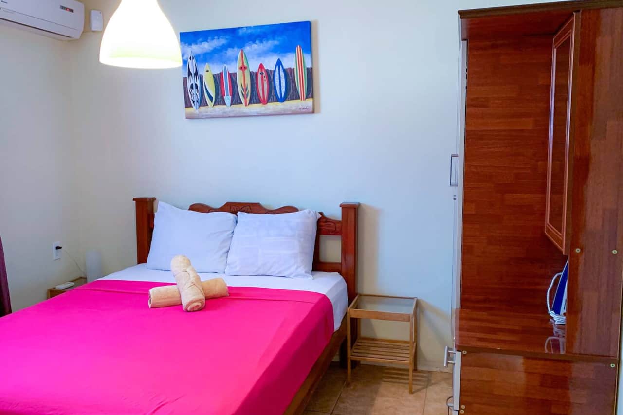 Air-conditioned bedroom with double bed, wardrobe, iron, ironing board, mirror, and towels. 
