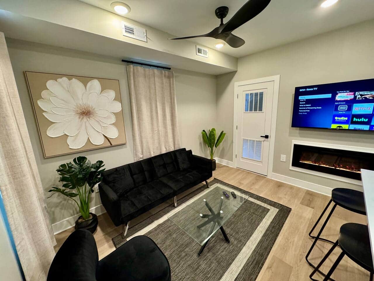 Modern kitchen featuring brand-new appliances, including a breakfast bar, dishwasher, microwave, and refrigerator. It seamlessly connects to the living room, which is furnished with a sofa bed, ana a large flat-screen TV.
