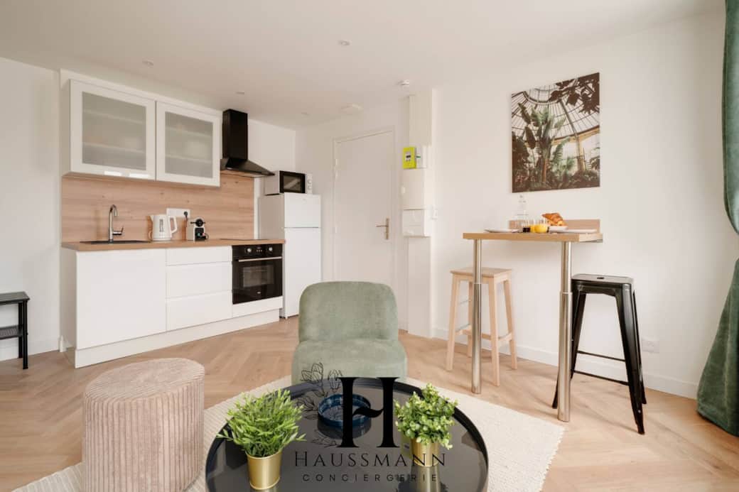  Cuisine moderne ouverte, équipée d’un four, plaques, hotte, micro-ondes, bouilloire et vaisselle complète. Espace repas convivial avec table haute et tabourets, idéal pour cuisiner et partager un moment chaleureux.