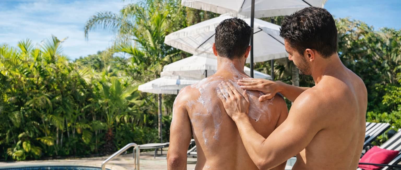 A friend applying sunscreen to another man by the pool at Casa Citron, reflecting a relaxed, supportive, and masculine atmosphere at a private gay men’s guesthouse in Fort Lauderdale.