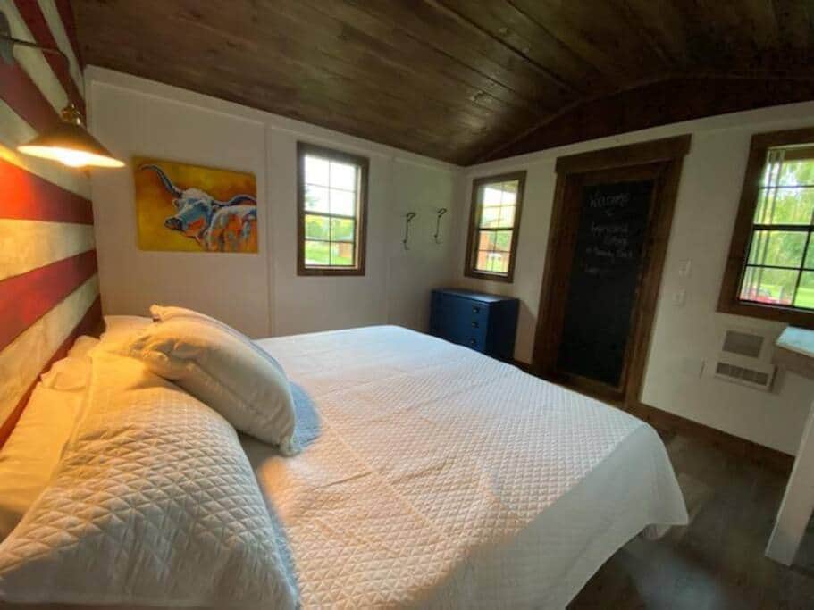 A king size bed, dresser, table, and mini fridge.