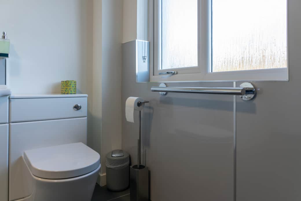 Spotlessly clean toilet, shower, and sink, with toilet paper, towel, mat, and toiletries provided.